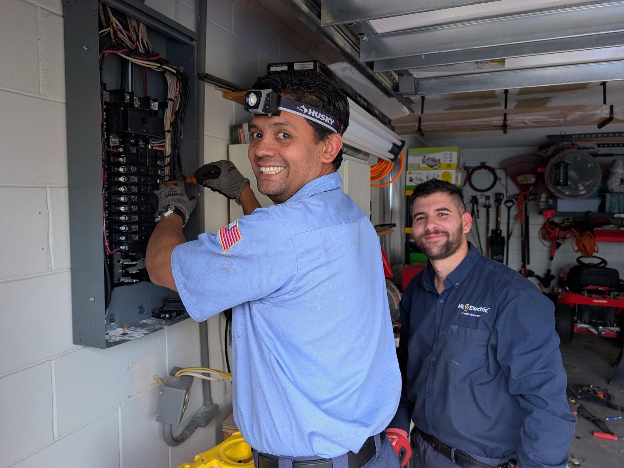 Two Mr. Electric technicians working at a residential electrical panel